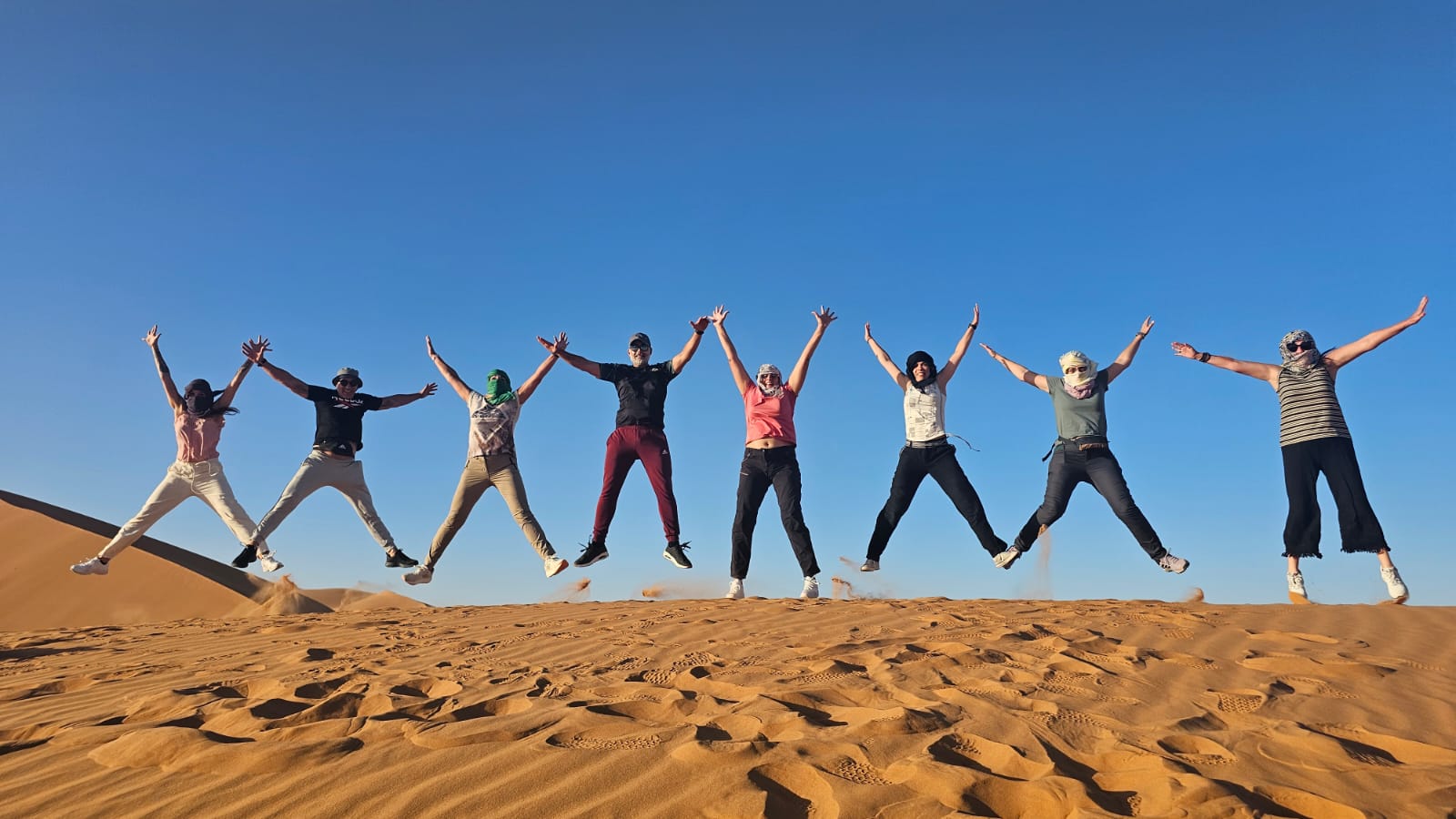 Viajeros saltando y divirtiéndose en las dunas de arena del Sáhara, un momento de pura felicidad de nuestros viajes.